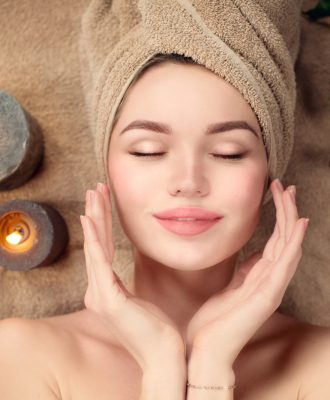 Beautiful spa woman with a towel on her head lying and touching face skin. Skincare. Beauty smiling model girl in spa salon
